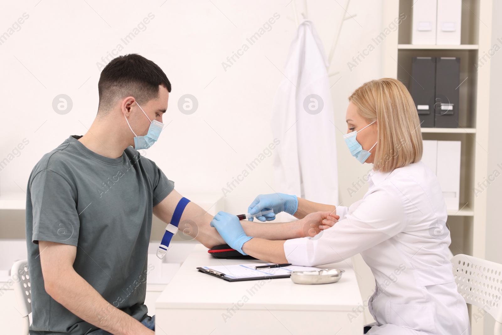 Photo of Doctor taking blood sample from patient with syringe at white table in hospital