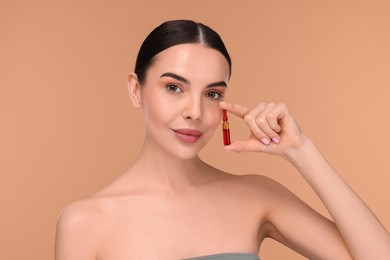 Photo of Beautiful young woman holding skincare ampoule on beige background