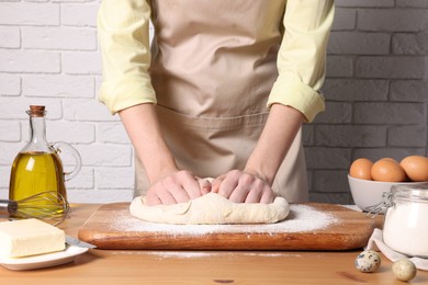 Woman kneading dough at wooden table near white brick wall, closeup