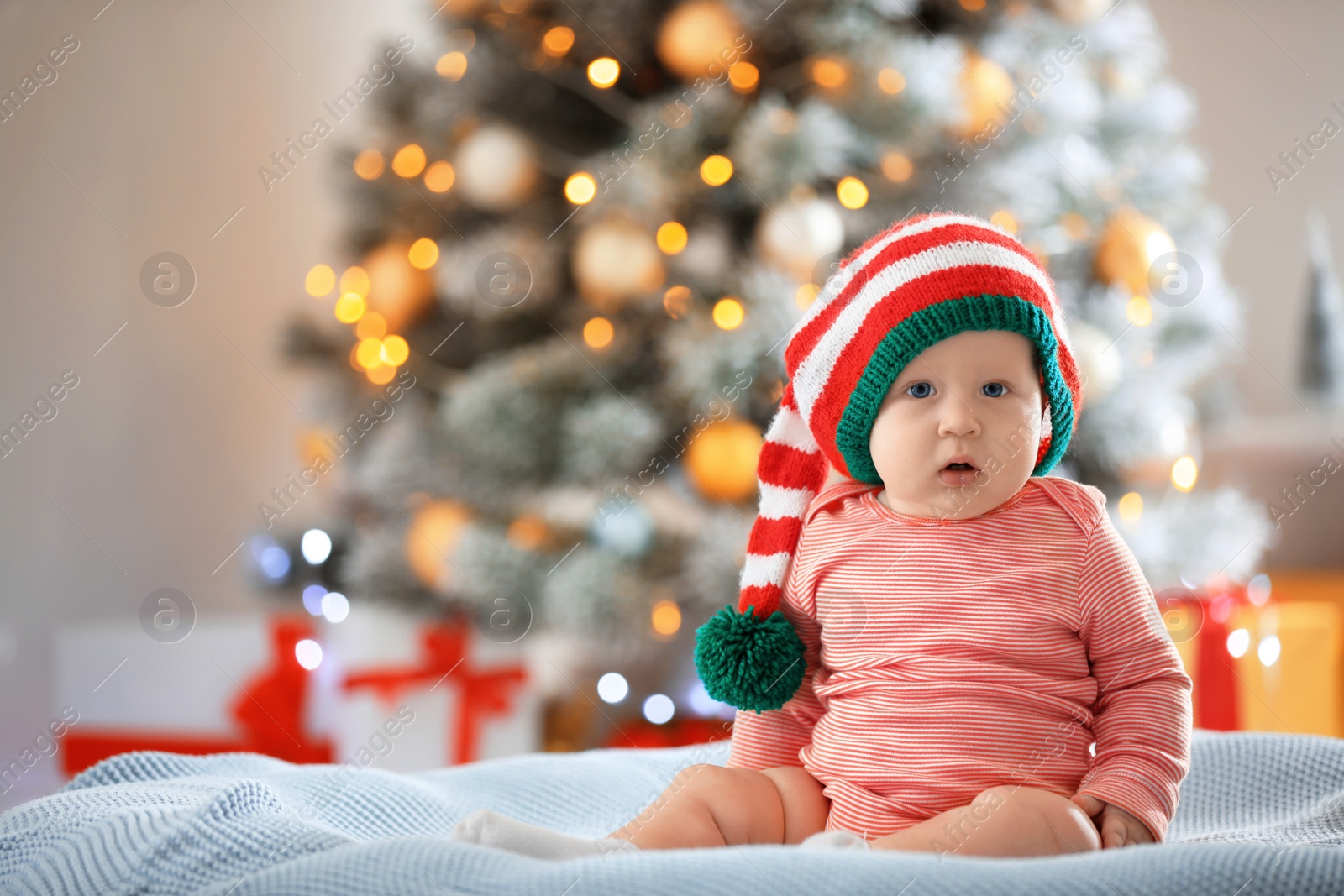 Photo of Little baby wearing elf hat on blanket indoors. First Christmas