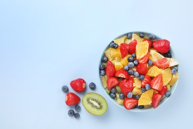 Photo of Yummy fruit salad in bowl and ingredients on light blue background, flat lay