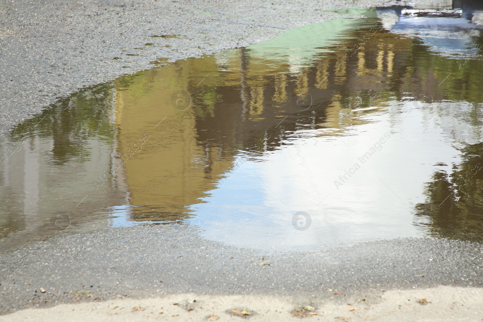 Photo of Reflection of buildings in rippled puddle water on asphalt