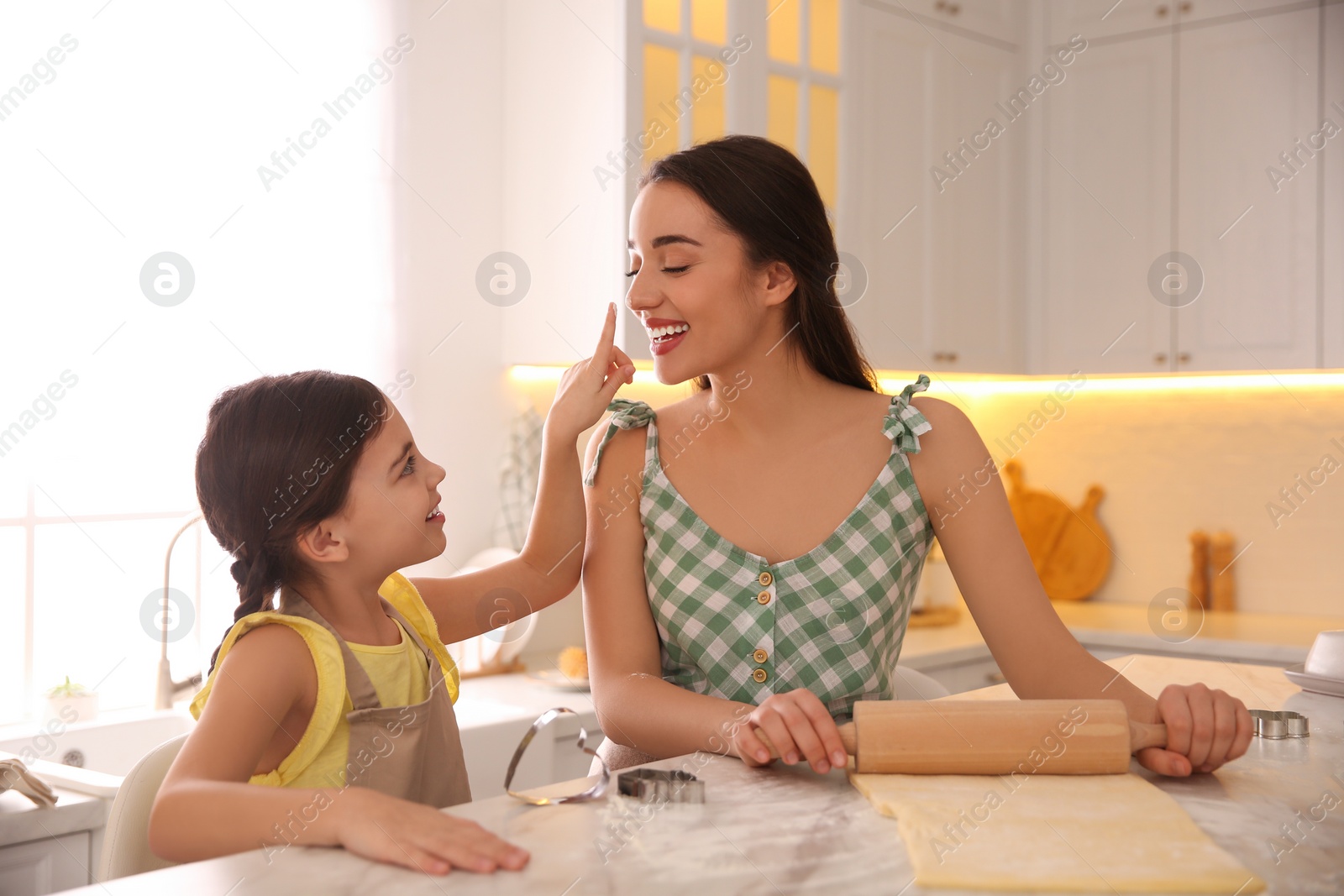 Photo of Mother with her cute little daughter having fun while rolling dough in kitchen