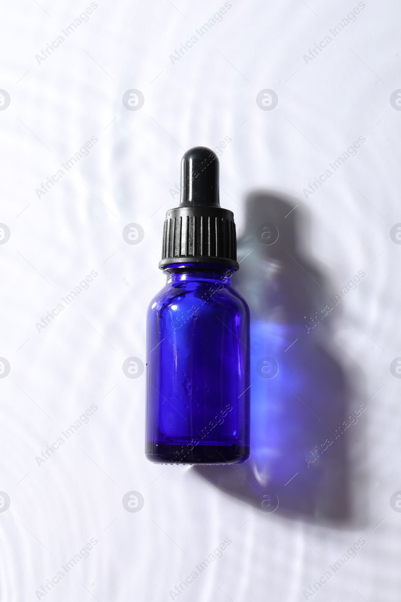 Photo of Bottle of face serum in water on white background, top view