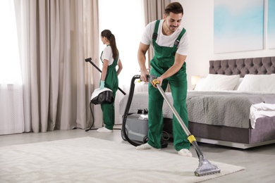 Team of janitors cleaning bedroom with professional equipment