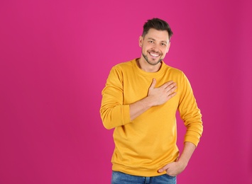 Portrait of handsome man holding hand near his heart on color background, space for text