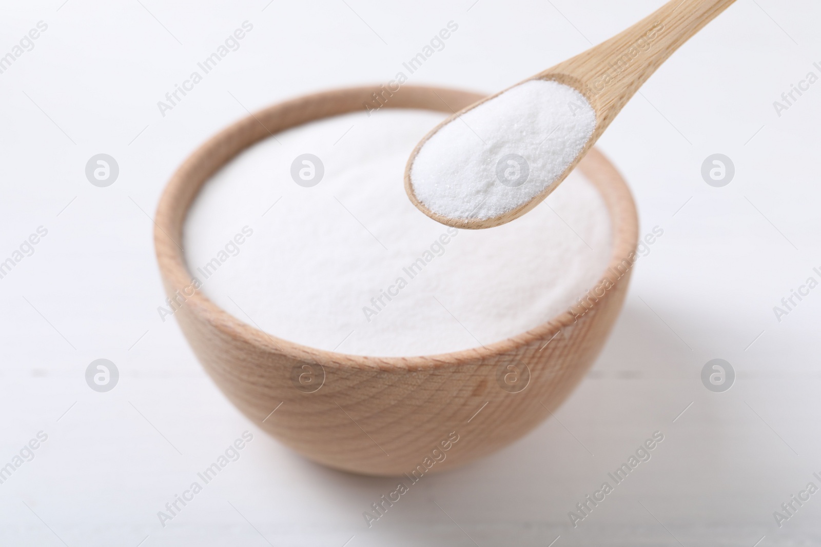 Photo of Taking baking soda from bowl at white wooden table, closeup