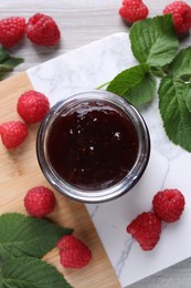 Photo of Delicious raspberry jam, fresh berries and green leaves on light table, flat lay