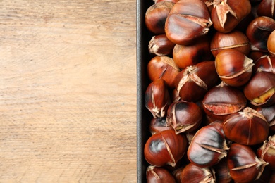 Photo of Delicious roasted edible chestnuts in baking dish on wooden table, top view. Space for text