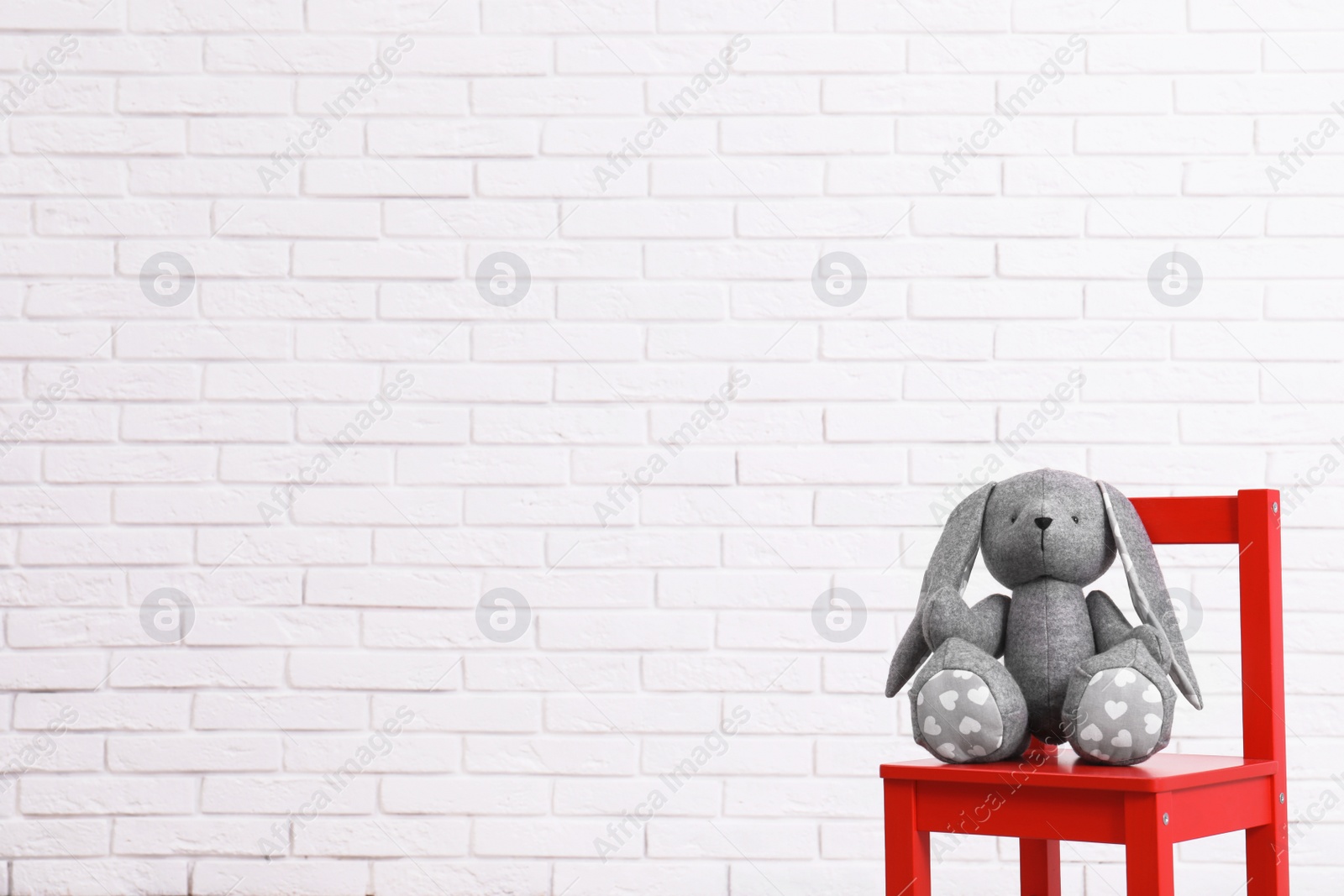 Photo of Stuffed toy rabbit on chair against white brick wall, space for text. Child room interior details