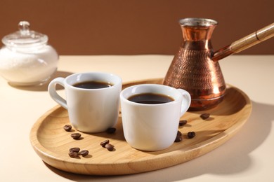 Photo of Delicious coffee in cups, beans and cezve on beige table, closeup