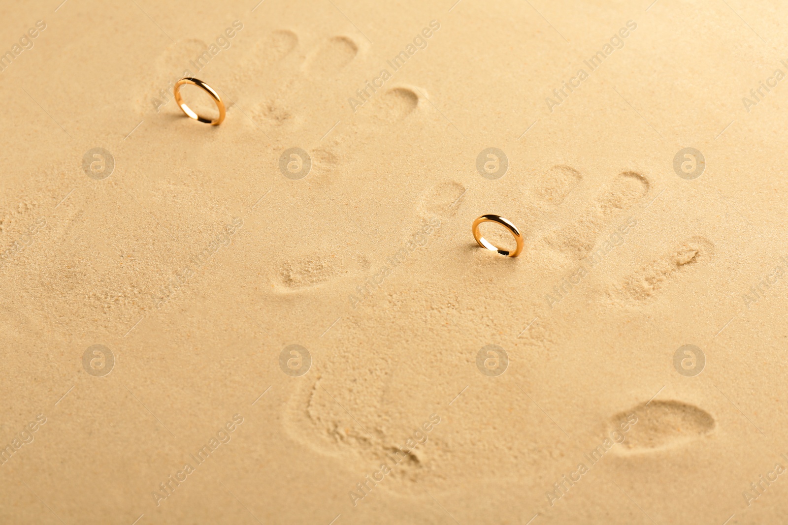 Photo of Honeymoon concept. Handprints and two golden rings on sand, above view