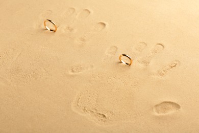 Photo of Honeymoon concept. Handprints and two golden rings on sand, above view