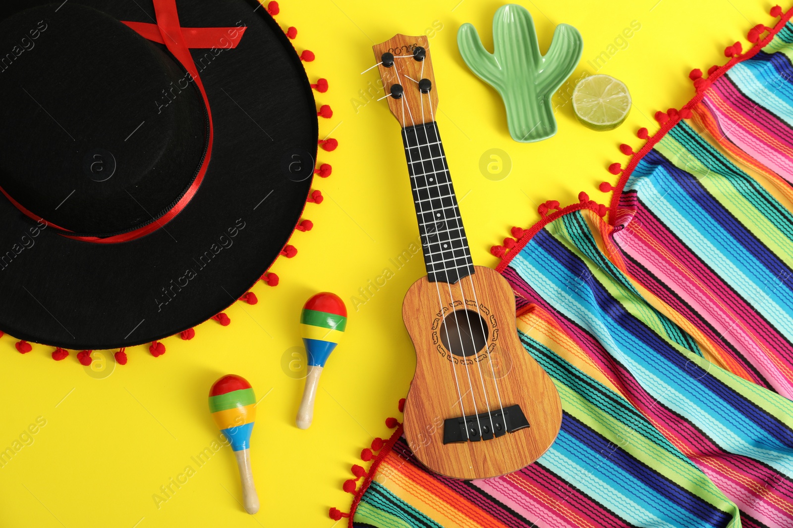 Photo of Flat lay composition with black Flamenco hat, poncho, ukulele and maracas on yellow table