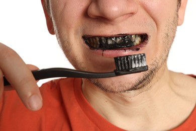 Photo of Man brushing teeth with charcoal toothpaste on white background, closeup