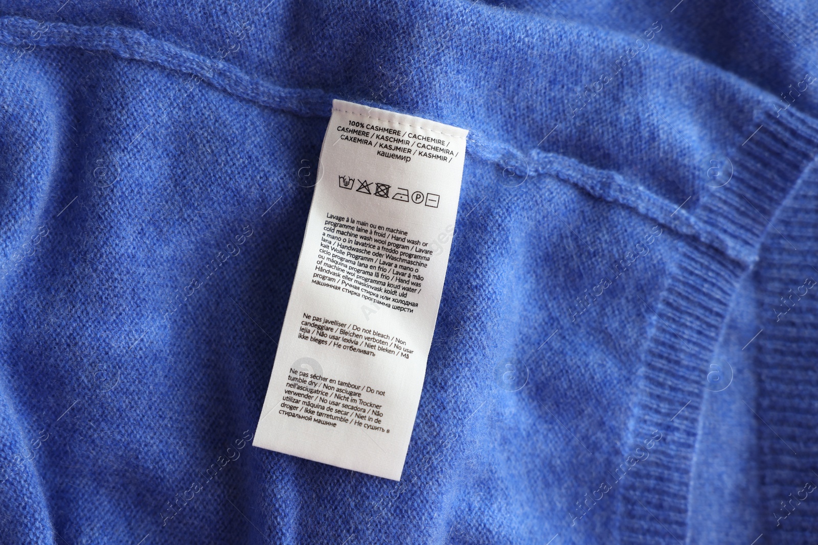 Photo of Clothing label in different languages on blue garment, top view