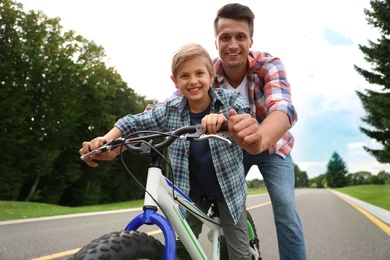 Image of Dad teaching son to ride bicycle outdoors