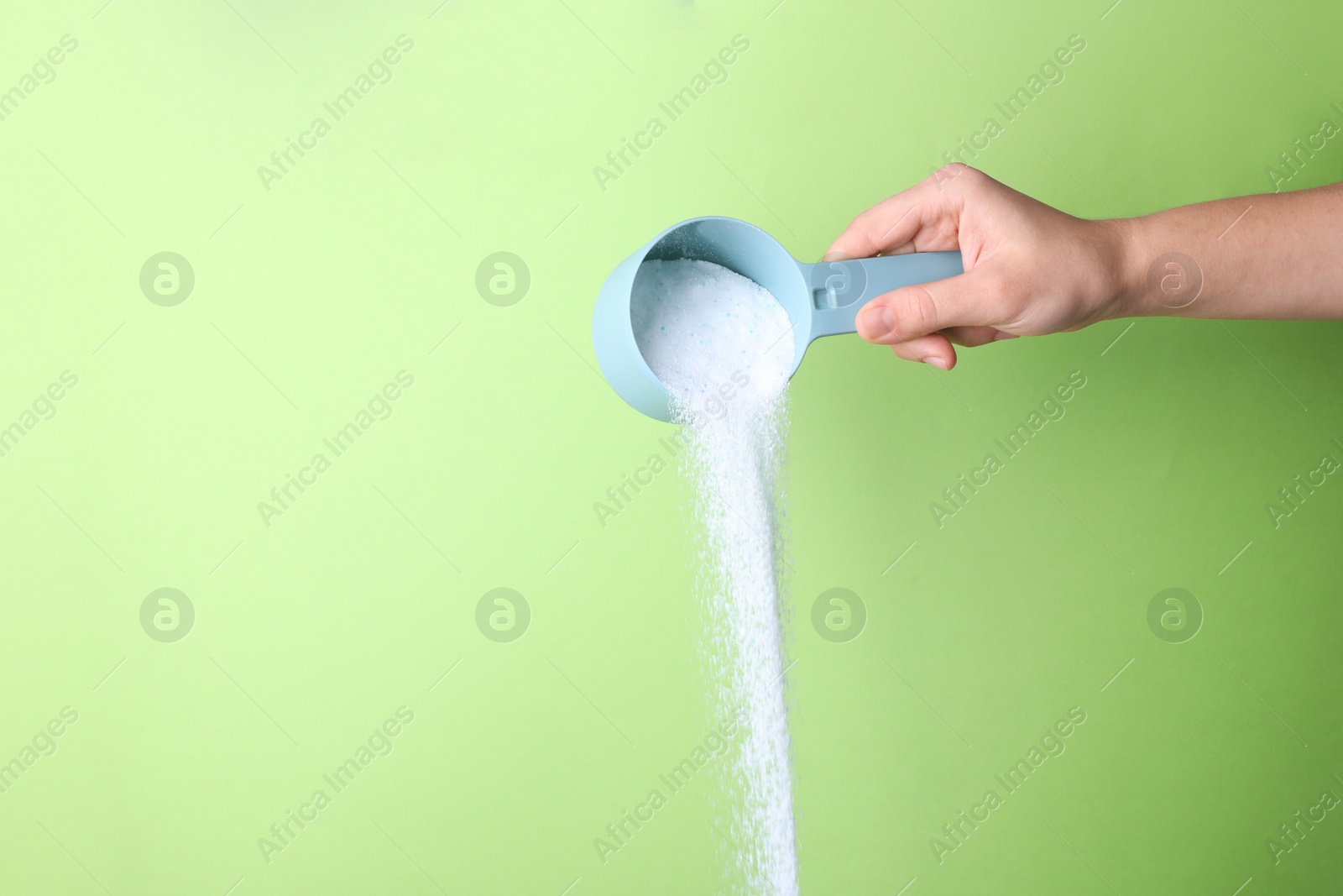 Photo of Woman pouring laundry detergent from measuring container against green background, closeup. Space for text