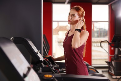Athletic young woman with earphones training on treadmill in gym
