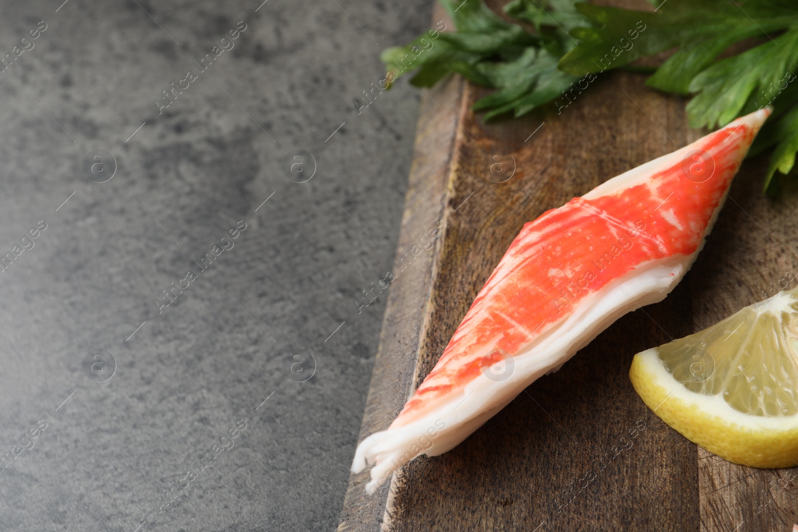 Photo of Piece of crab stick and lemon slice on grey table, closeup. Space for text