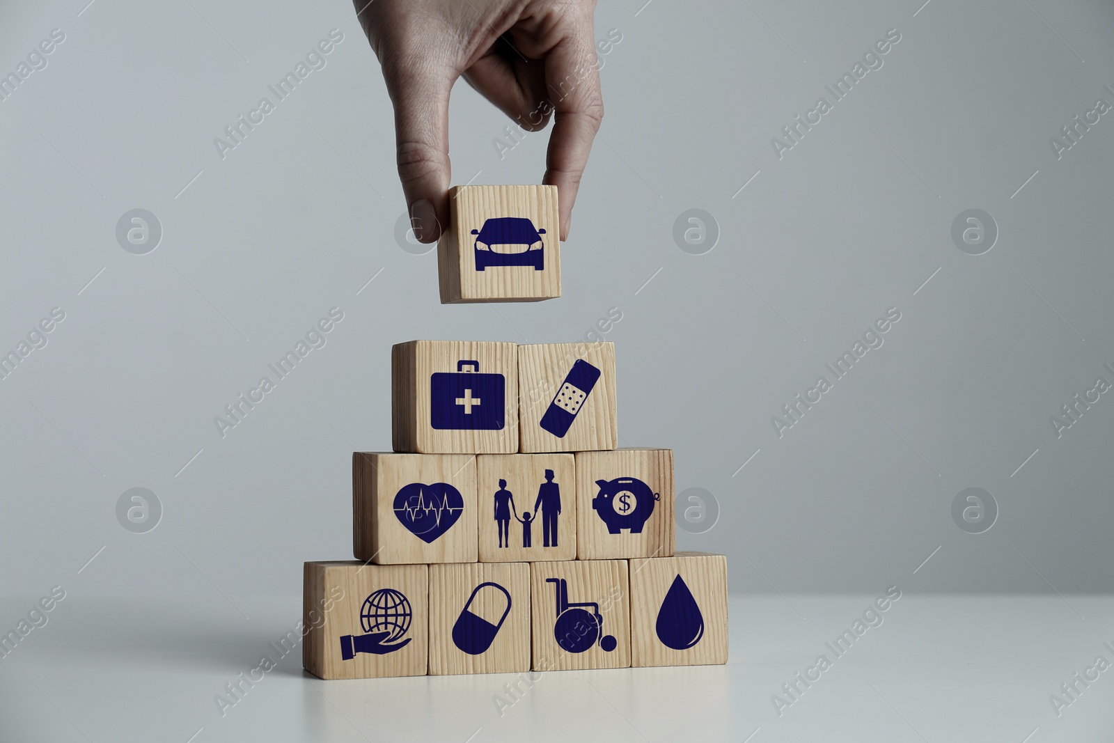 Image of Woman building pyramid of wooden cubes with different icons at white table indoors, closeup. Insurance concept