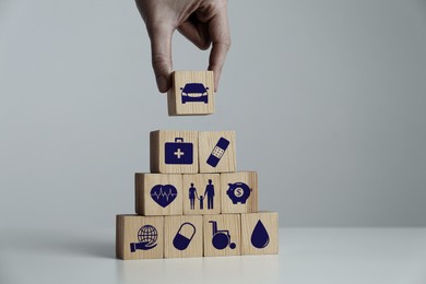 Image of Woman building pyramid of wooden cubes with different icons at white table indoors, closeup. Insurance concept