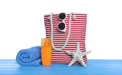 Stylish bag, starfish and other beach accessories on light blue wooden table against white background