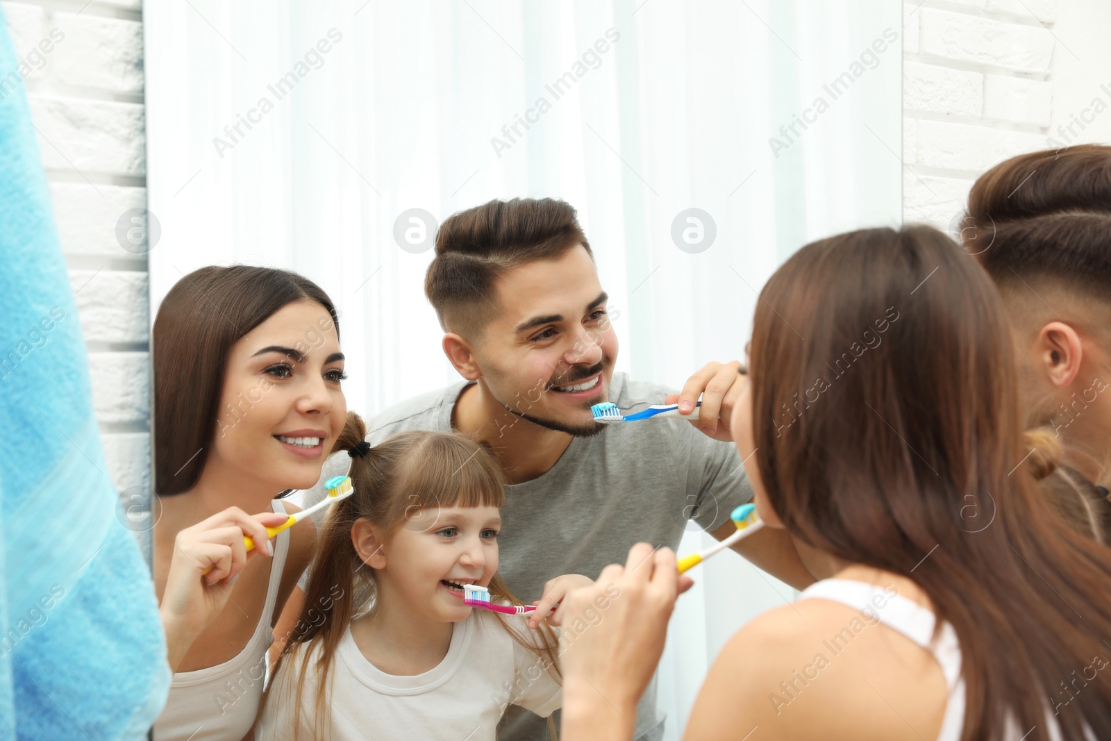 Photo of Little girl and her parents brushing teeth together near mirror in bathroom at home