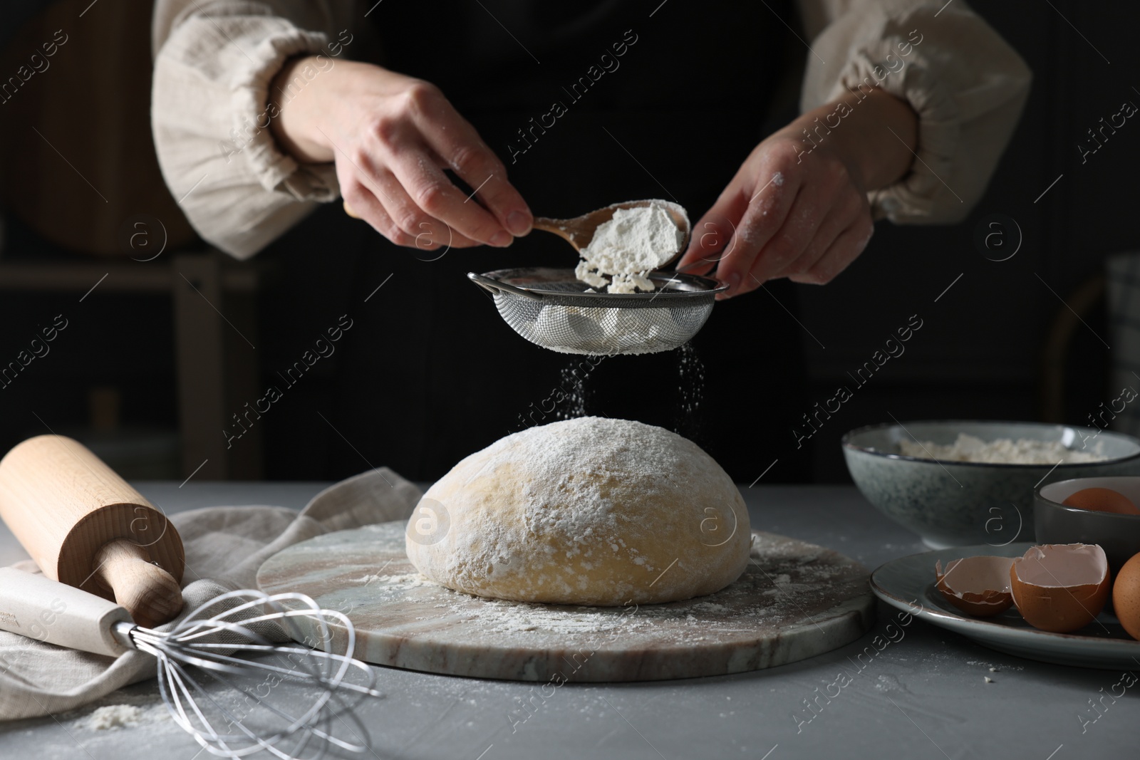 Photo of Making dough. Woman sifting flour at grey table, closeup