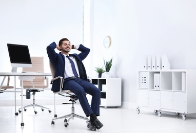 Photo of Young businessman sitting on office chair at workplace, space for text