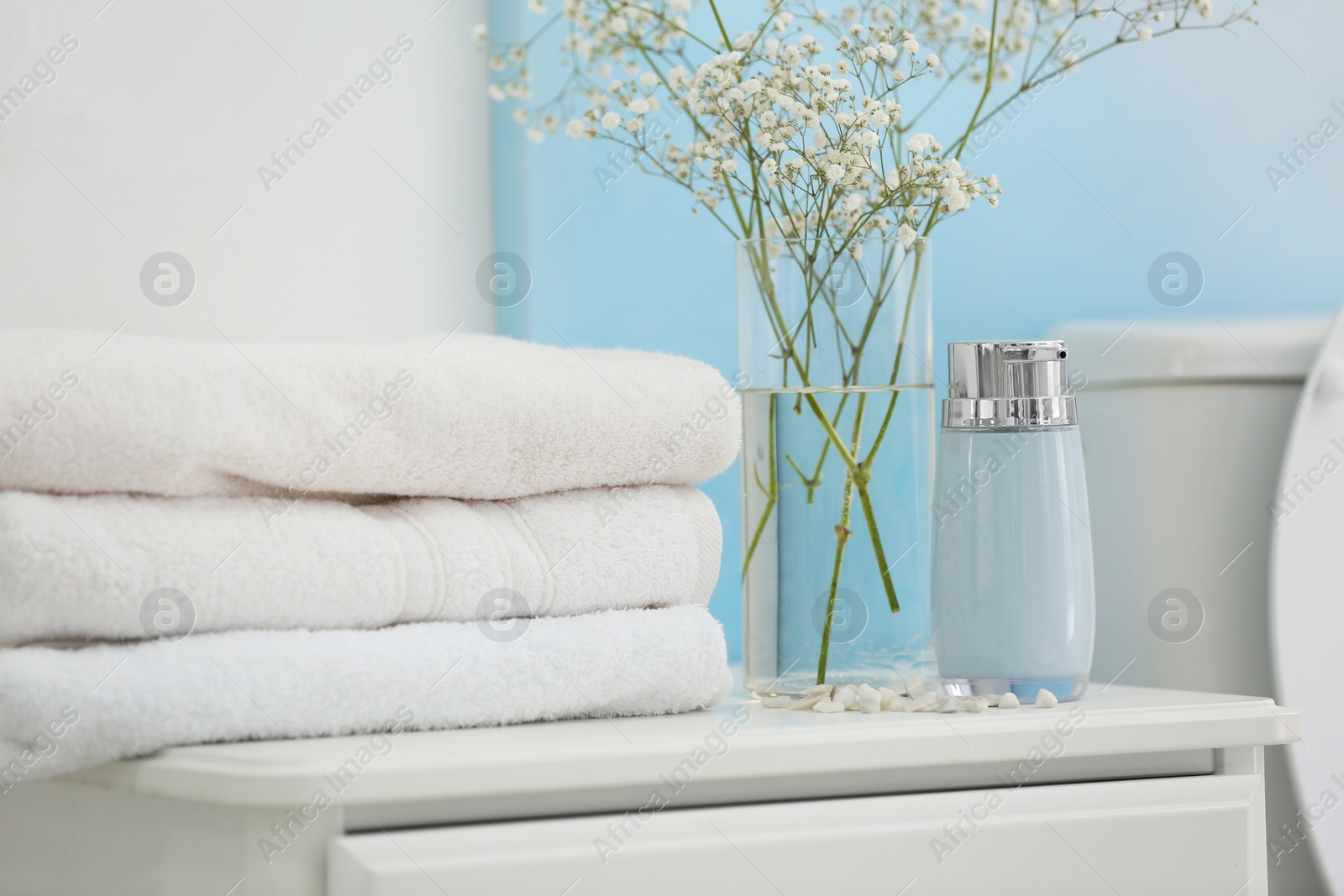 Photo of Fresh clean towels, soap dispenser and flowers on cabinet in bathroom
