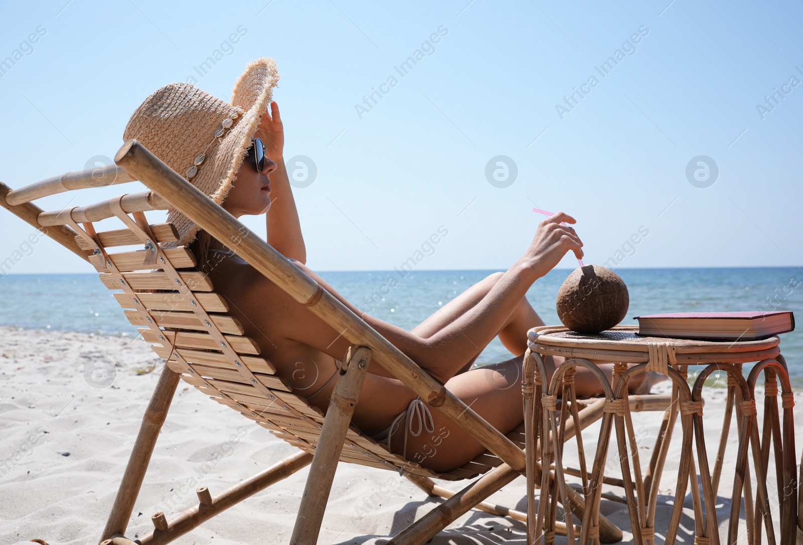 Photo of Woman with cocktail resting in wooden sunbed on tropical beach