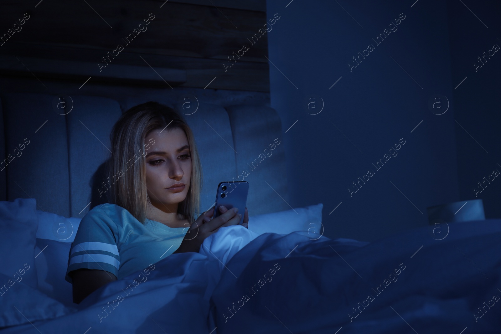 Photo of Young woman using smartphone in bed at night. Nomophobia and sleeping disorder problem