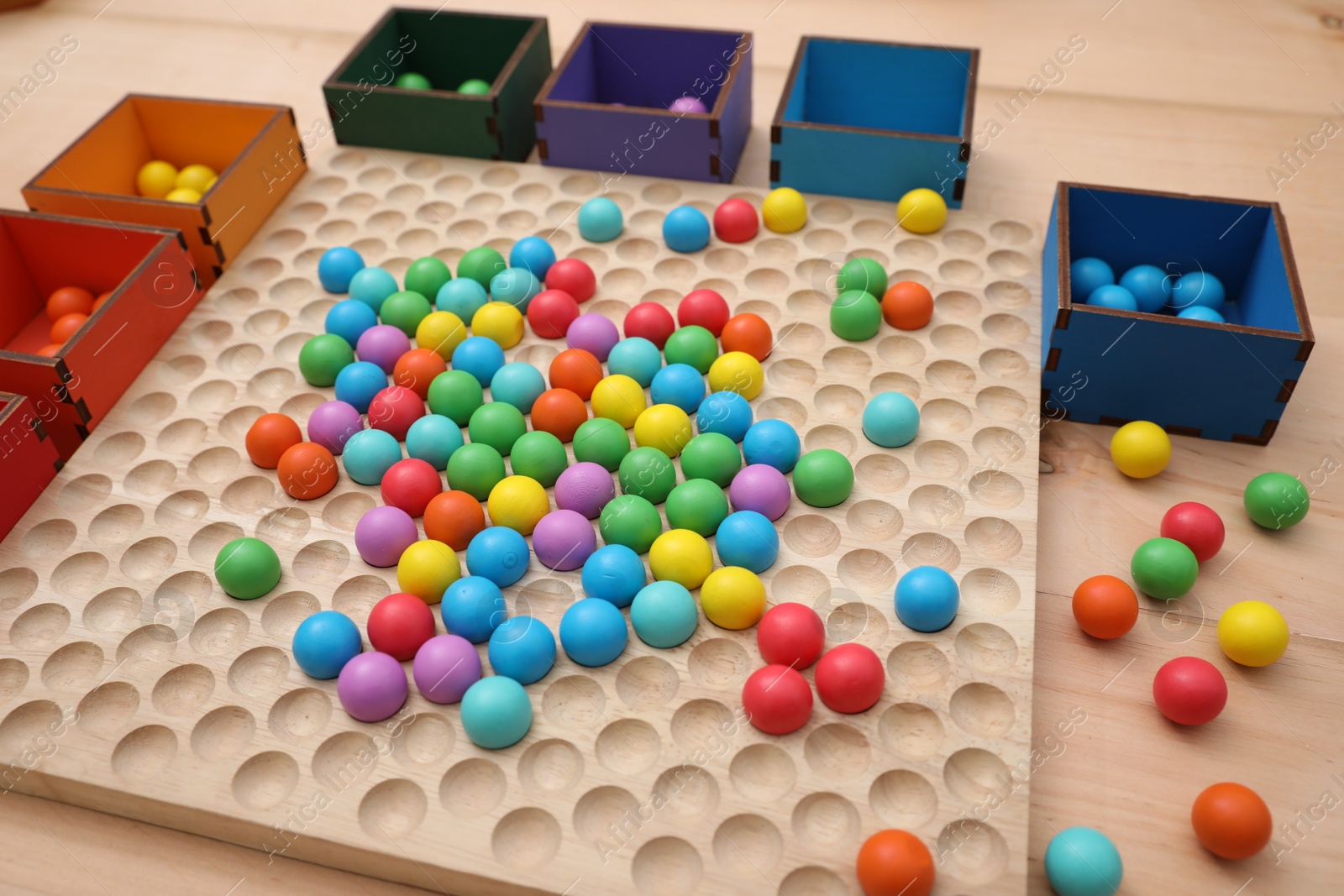 Photo of Wooden sorting board and boxes with colorful balls on table, closeup. Montessori toy