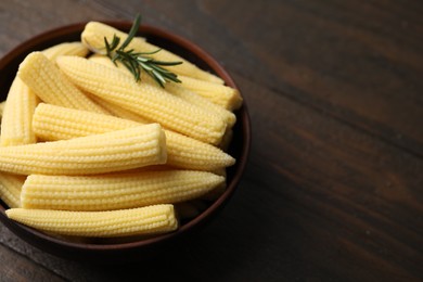 Photo of Tasty fresh yellow baby corns in bowl on wooden table, closeup. Space for text