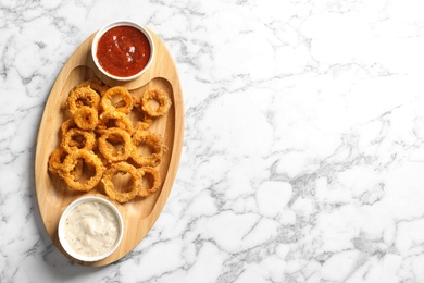 Homemade crunchy fried onion rings with sauces on marble table, top view. Space for text