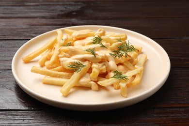 Photo of Delicious french fries with cheese sauce and dill on wooden table, closeup