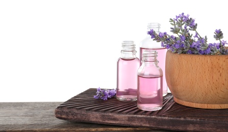 Photo of Bottles of lavender essential oil and bowl with lavender flowers on wooden table against white background