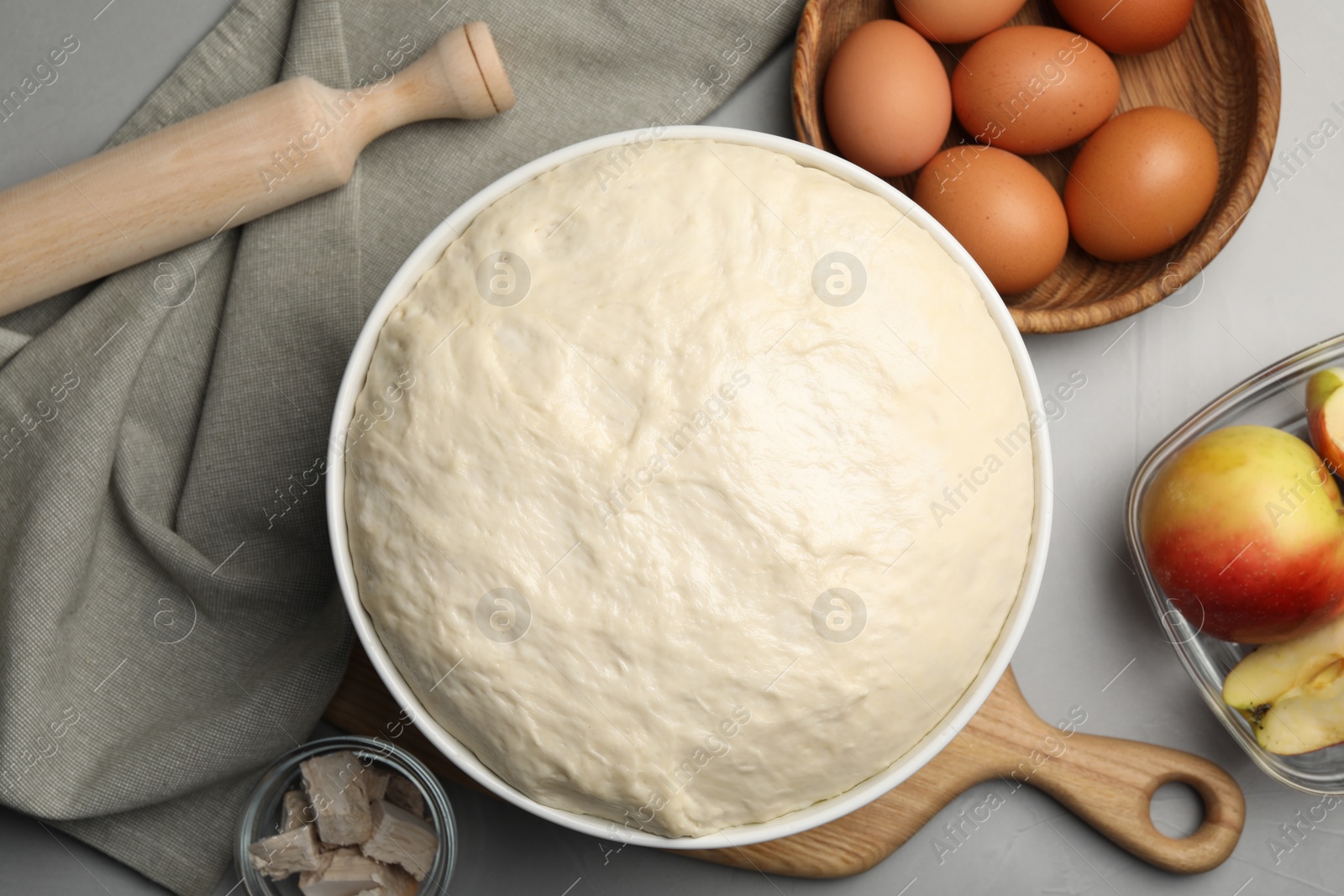 Photo of Fresh dough, rolling pin and ingredients on grey table, flat lay. Cooking yeast cake