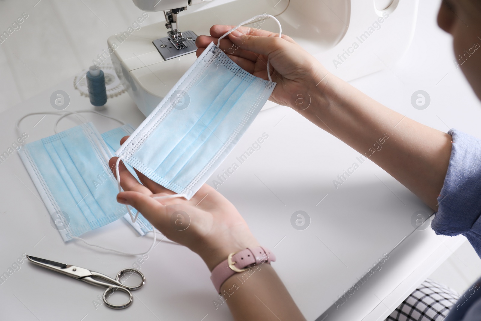 Photo of Woman sewing disposable protective mask with machine at table, closeup