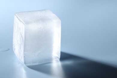 Crystal clear ice cube on light blue background, closeup. Space for text
