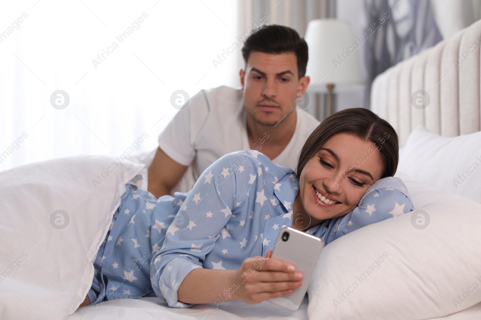 Photo of Distrustful man peering into girlfriend's smartphone at home. Jealousy in relationship