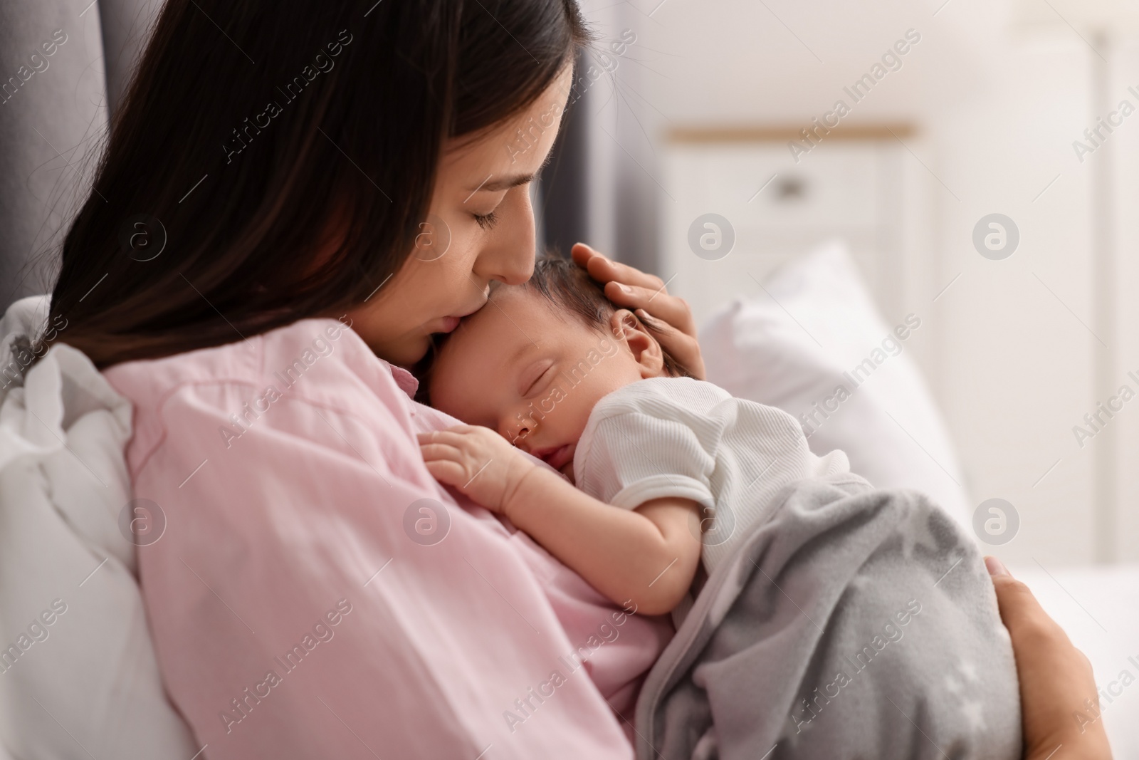 Photo of Mother kissing her sleeping newborn baby in bed at home