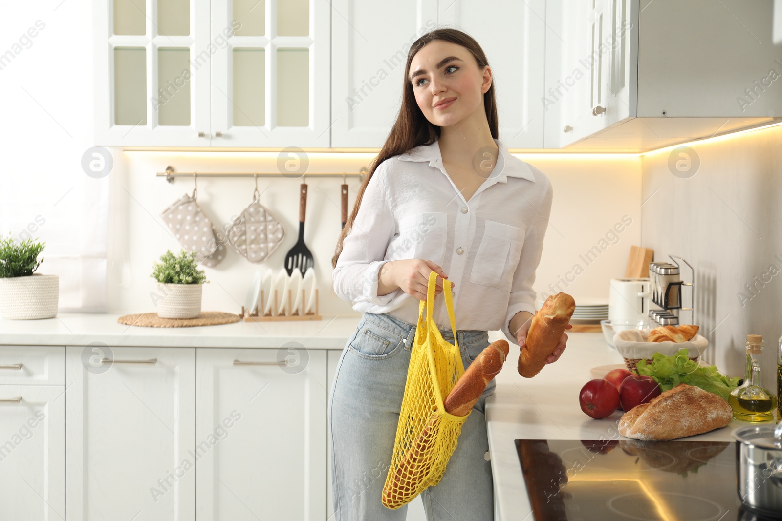 Photo of Woman holding string bag with baguettes in kitchen