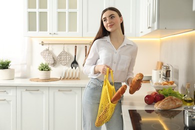 Woman holding string bag with baguettes in kitchen