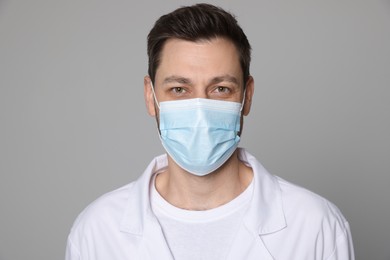 Photo of Doctor or medical assistant (male nurse) in uniform with protective mask on light grey background