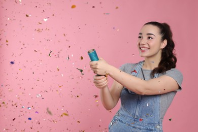 Young woman blowing up party popper on pink background