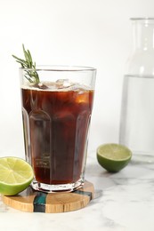 Photo of Refreshing iced coffee with rosemary in glass and fresh lime on white marble table