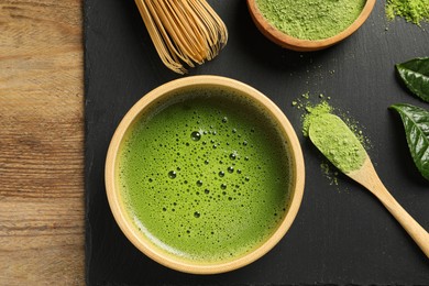 Photo of Cup of fresh matcha tea, green powder and bamboo whisk on wooden table, top view