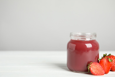 Healthy baby food in jar and fresh strawberries on white wooden table against grey background. Space for text